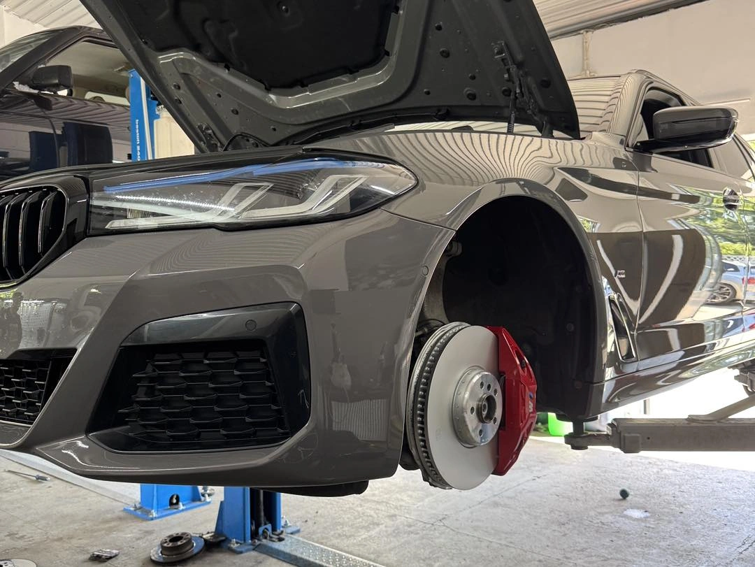 Szary BMW na podnośniku, widoczne czerwone zaciski hamulcowe.