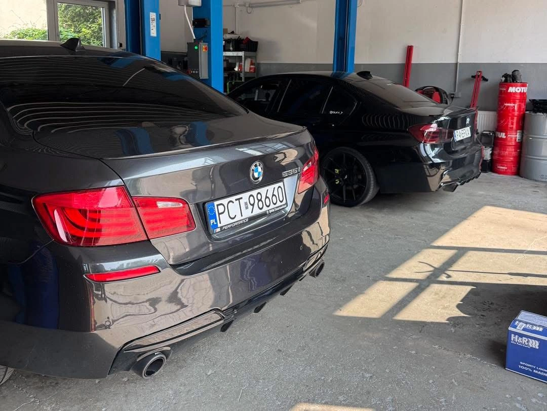 Dwa czarne BMW w serwisie, widok od tyłu z widocznymi numerami rejestracyjnymi.